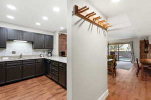Kitchen with light wood finished floors, tasteful backsplash, black dishwasher, a textured wall, and light stone countertops