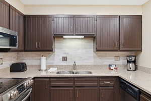 Kitchen featuring light stone counters, stainless steel appliances, dark wood finish cabinetry, and decorative backsplash