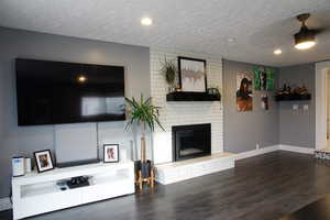 Living room with a textured ceiling, dark wood finished floors, and a fireplace