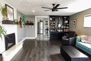 Living area featuring dark wood-style flooring, a ceiling fan, a textured ceiling, and a fireplace