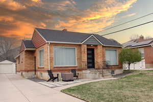 View of front of house featuring a front yard, a detached garage, brick siding, an outbuilding, and roof with shingles