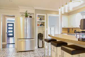 Kitchen with freestanding refrigerator, ornamental molding, light countertops, a breakfast bar area, and hanging light fixtures