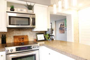 Kitchen featuring stainless steel appliances, white cabinets, tasteful backsplash, and hanging light fixtures