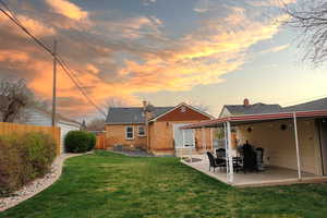 Back of property at dusk with a chimney, brick siding, a patio area, a fenced backyard, and roof with shingles