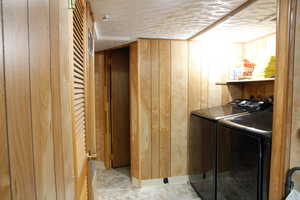Laundry room with wooden walls, separate washer and dryer, and a textured ceiling