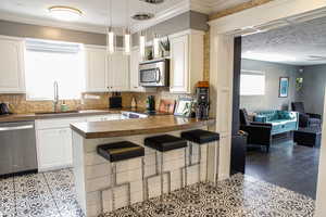 Kitchen with dark countertops, a kitchen bar, stainless steel appliances, a peninsula, and white cabinets