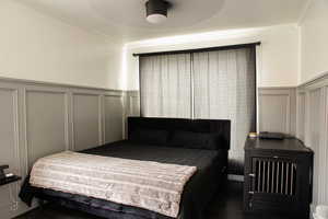 Bedroom featuring a decorative wall, crown molding, a wainscoted wall, wood finished floors, and a ceiling fan