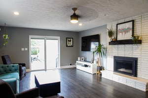 Living room with dark wood-style floors, a textured ceiling, and a brick fireplace