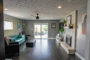 Living area with ceiling fan, dark wood finished floors, a fireplace, a textured ceiling, and recessed lighting