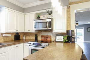 Kitchen featuring white cabinetry, stainless steel appliances, ornamental molding, decorative backsplash, and dark countertops