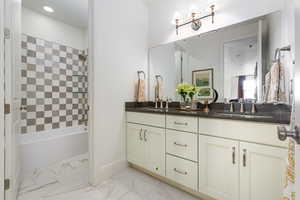 Bathroom featuring double vanity, shower / bath combination, and light marble finish flooring