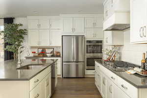 Kitchen with stainless steel appliances, dark wood-style floors, dark stone counters, white cabinetry, and tasteful backsplash