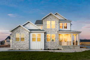 View of front of property featuring stone siding, covered porch, board and batten siding, and a front lawn