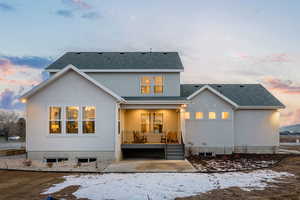 Back of property at dusk with stucco siding, a shingled roof, and a patio area