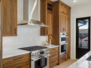 Kitchen with stainless steel appliances, wood finish cabinets, light stone countertops, and backsplash