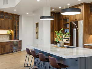 Kitchen featuring open shelves, glass fronted cabinets, light stone counters, high quality fridge, and light wood-style flooring