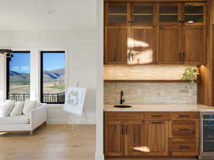 Indoor wet bar featuring wood finish cabinetry, decorative backsplash, beverage cooler, a mountain view, and light wood-type flooring