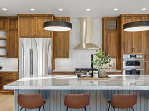 Kitchen featuring stainless steel appliances, wood finish cabinetry, light stone countertops, tasteful backsplash, and a kitchen bar