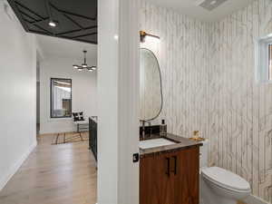 Half bathroom with vanity, light wood finished floors, and wallpapered walls