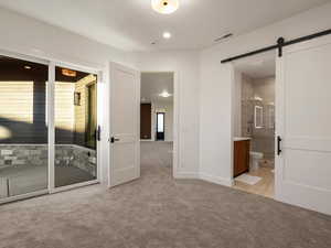 Unfurnished bedroom featuring light colored carpet, ensuite bathroom, a barn door, and recessed lighting
