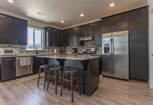 Kitchen featuring stainless steel appliances, a breakfast bar, a kitchen island, dark wood finish cabinetry, and light wood-style flooring