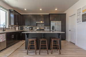 Kitchen featuring a breakfast bar area, dark wood finish cabinets, stainless steel appliances, a kitchen island, and recessed lighting