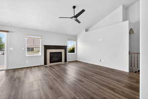Unfurnished living room featuring ceiling fan, lofted ceiling, a tile fireplace, and dark wood-style floors