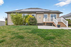 Back of property featuring stucco siding, solar panels, a patio, a deck, and a shingled roof