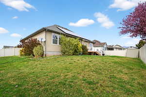 Rear view of house with a fenced backyard, a wooden deck, roof mounted solar panels, and stucco siding