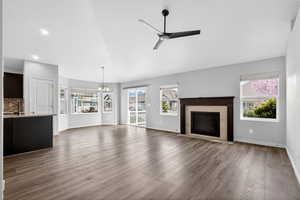 Unfurnished living room with a ceiling fan, a fireplace, a chandelier, dark wood finished floors, and vaulted ceiling