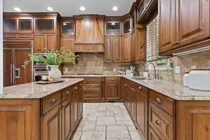 Kitchen featuring glass insert cabinets, wood finish cabinets, light stone countertops, paneled refrigerator, and stone tile flooring