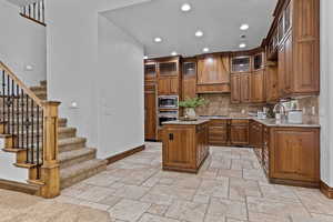 Kitchen featuring wood finish cabinets, light stone countertops, glass insert cabinets, a center island, and recessed lighting