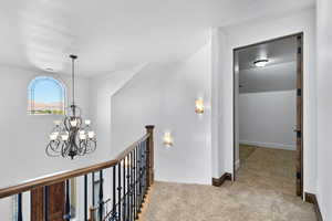Hall with light colored carpet, a chandelier, and an upstairs landing