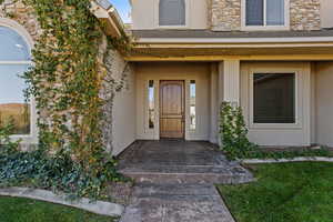 Entrance to property featuring stucco siding, covered porch, and stone siding