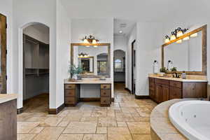 Full bath featuring a spacious closet, two vanities, stone tile floors, a whirlpool tub, and recessed lighting