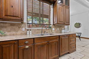 Kitchen featuring light stone counters, glass fronted cabinets, wood finish cabinetry, stone tile flooring, and decorative backsplash