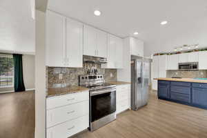 Two tone kitchen with stainless steel appliances, light wood-style flooring, dual tone cabinetry, backsplash, and wood counters