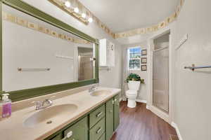 Full bathroom featuring a shower stall, double vanity, dark wood-style floors, and a textured ceiling