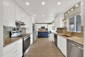 Kitchen with stainless steel appliances, two tone color scheme, open shelves, recessed lighting, and light stone countertops