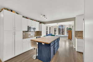 Kitchen with butcher block counters, a kitchen breakfast bar, a kitchen island, two tone cabinets, and light wood-type flooring