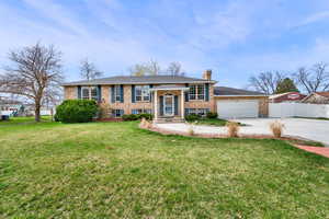 Raised ranch featuring concrete driveway, a chimney, brick siding, and a garage