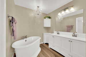 Bathroom with double vanity, a freestanding tub, light wood-style flooring, and suspended lighting