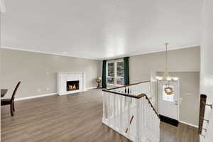 Unfurnished living room with hanging lights, crown molding, dark wood-style flooring, a warm lit fireplace, and a textured ceiling