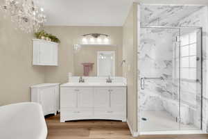 Full bathroom featuring a marble finish shower, double vanity, light wood-type flooring, a freestanding bath, and hanging lights