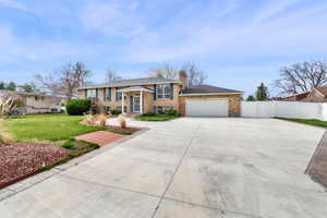 Raised ranch featuring driveway, brick siding, a garage, a gate, and a chimney