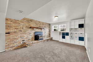 Unfurnished living room with carpet floors, a wood stove, a textured ceiling, and brick wall