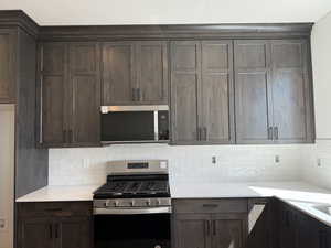 Kitchen with stainless steel appliances, dark wood finish cabinetry, decorative backsplash, and light stone countertops
