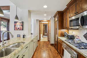 Kitchen with stainless steel appliances, decorative light fixtures, light stone countertops, dark wood-type flooring, and decorative backsplash
