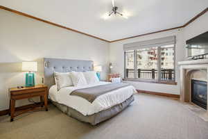 Bedroom featuring a fireplace with flush hearth, crown molding, and light colored carpet