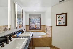 Full bath with two vanities, a textured ceiling, and a bath